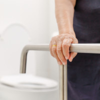 Elderly person using a grab bar to stand safely in the bathroom.